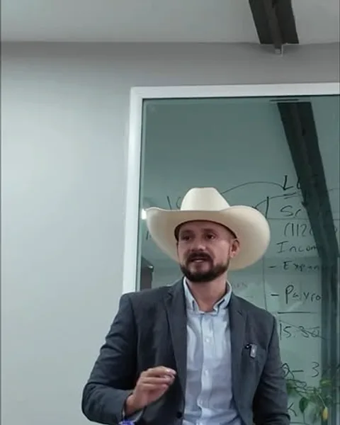 Marcos Ramirez explicando cifras frente a un tablero con cálculos de impuestos.